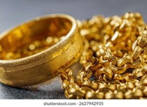 Närbild på en bred guldring och en glittrande guldkedja.