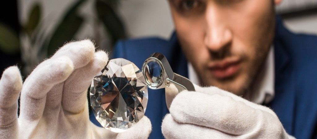 En juvelerare undersöker en stor slipad diamant med en lupp.